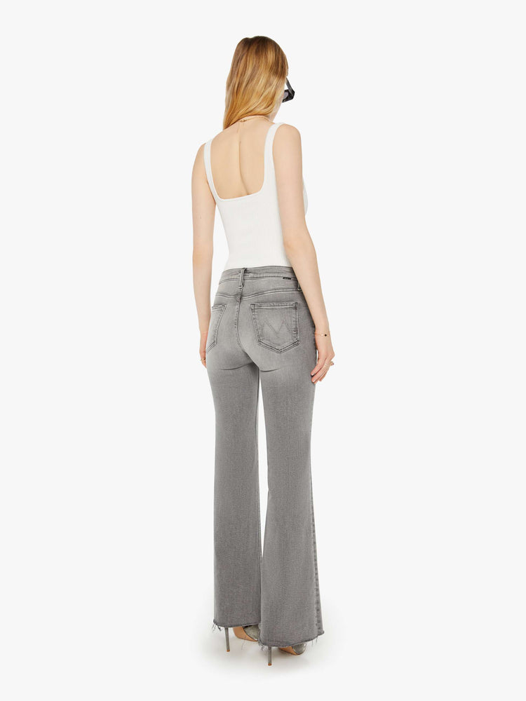 Back view of a woman in a light grey high rise flare  with a long 32-inch inseam, zip fly and a frayed hem. 