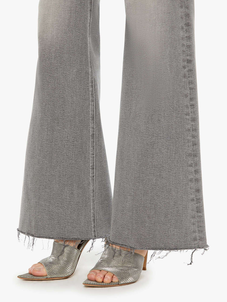 Hem view of a woman in a light grey high rise flare  with a long 32-inch inseam, zip fly and a frayed hem. 