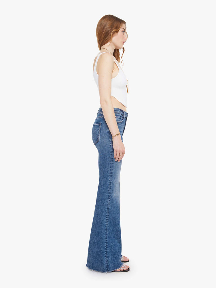Side view of a woman in a medium blue high-rise flare with a zip fly, long 32-inch inseam and a frayed hem.
