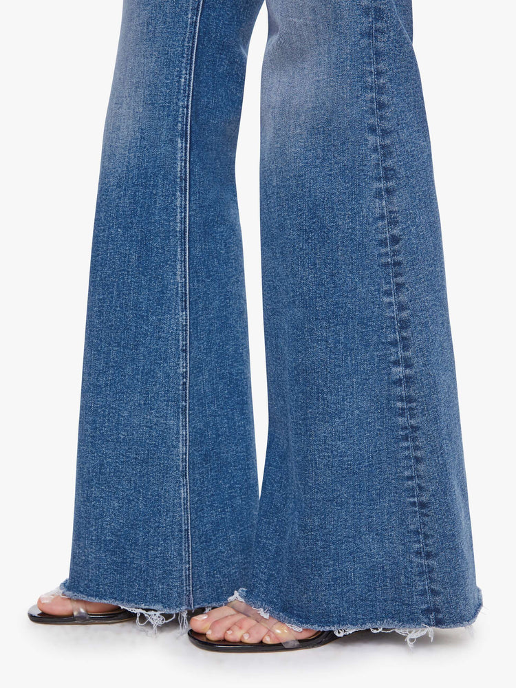 Hem view of a woman in a medium blue high-rise flare with a zip fly, long 32-inch inseam and a frayed hem.