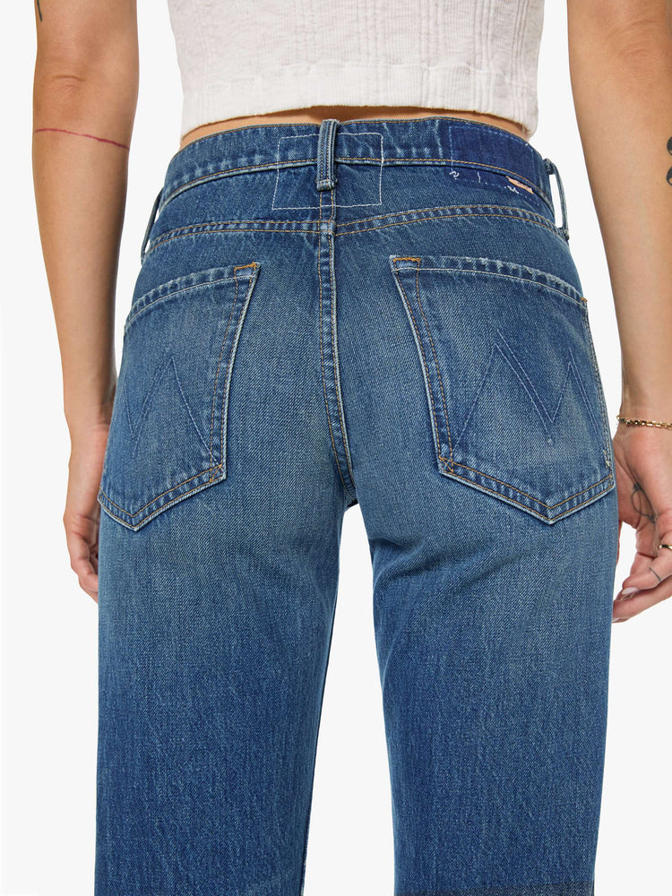 Back close view of a woman in a  straight leg with a bit of a kick, the jean features a mid rise, full-length inseam and clean hem in a classic blue.