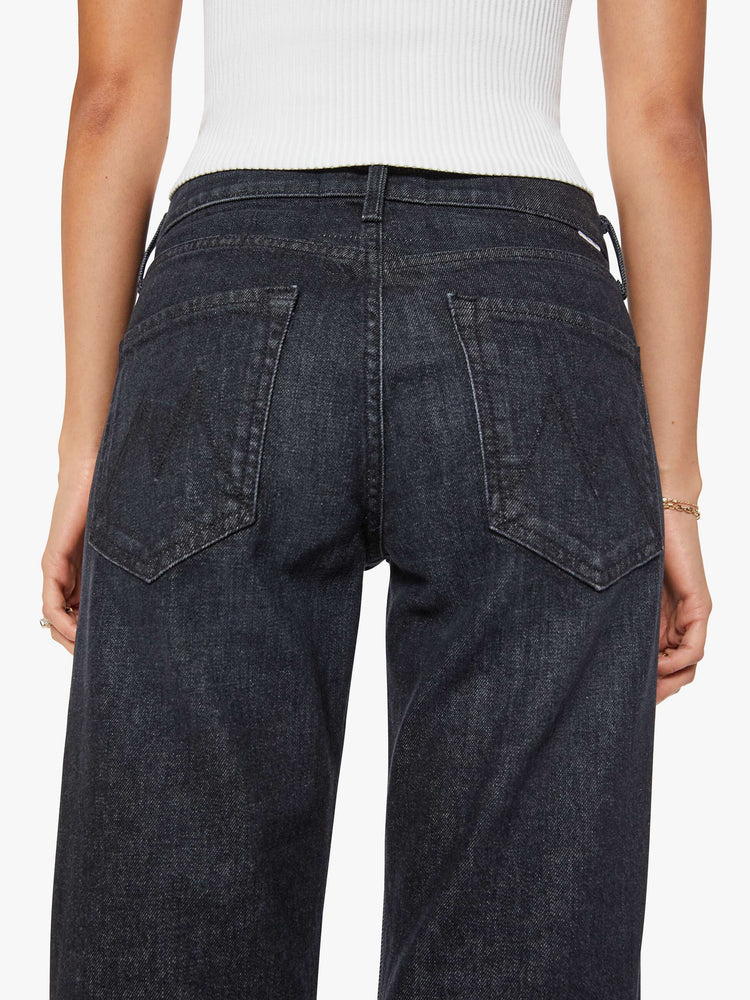 Close up view of a woman in black straight leg with a bit of a kick, the jean features a mid rise, full-length inseam, distressed hem and relaxed fit.