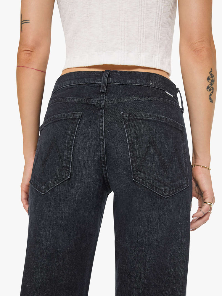Close up view of a woman in black straight leg with a bit of a kick, the jean features a mid rise, full-length inseam, distressed hem and relaxed fit.