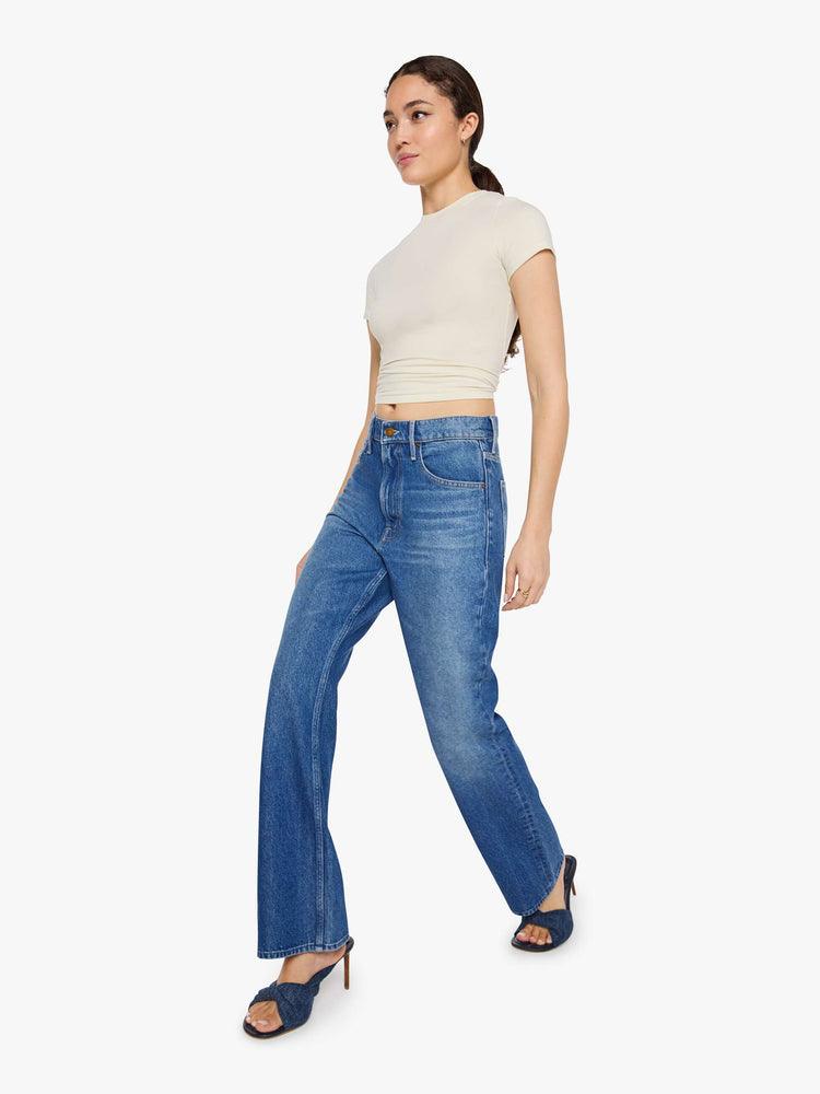 Walking view of a woman in a med blue low-slung jeans designed with a high rise, zip fly, a 32-inch inseam and a clean hem.