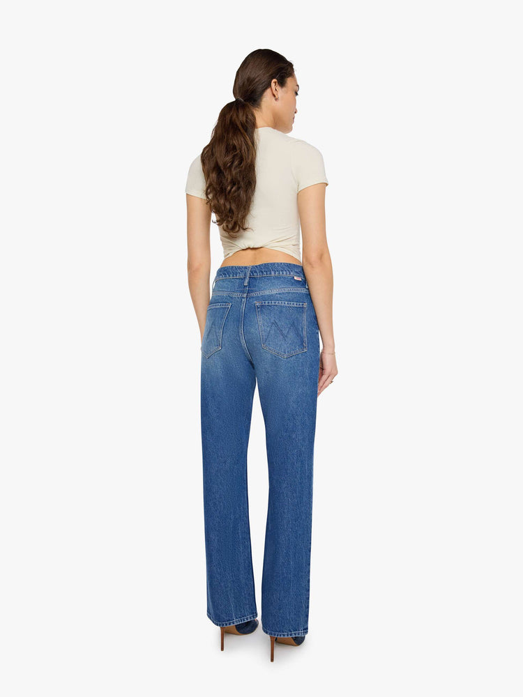 Back view of a woman in a med blue low-slung jeans designed with a high rise, zip fly, a 32-inch inseam and a clean hem.