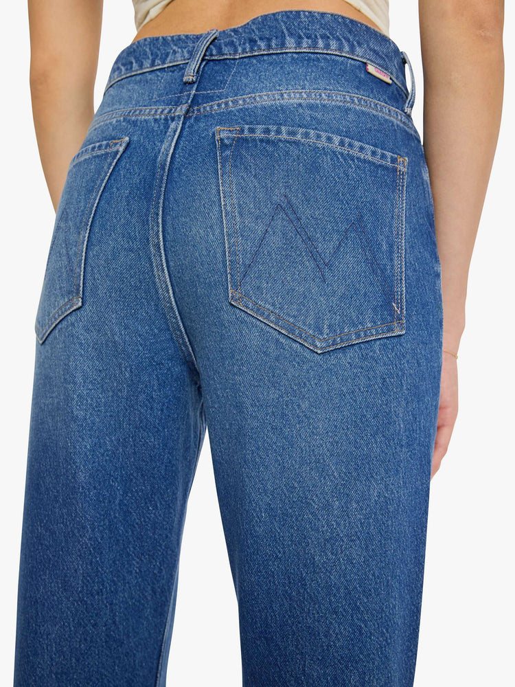 Close up view of a woman in a med blue low-slung jeans designed with a high rise, zip fly, a 32-inch inseam and a clean hem.