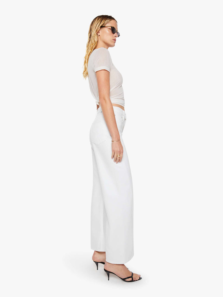 Side view of a woman in a white high-rise pants have a zip fly, loose wide leg with a curved outer seam and a 32-inch inseam with a clean hem.