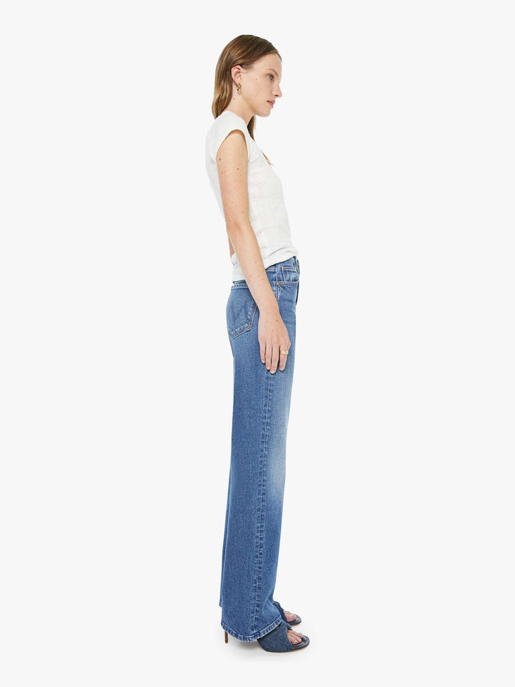 Side view of a woman in a med blue high-rise bootcut with a zip fly, looser leg and a long 32-inch inseam with a clean hem.