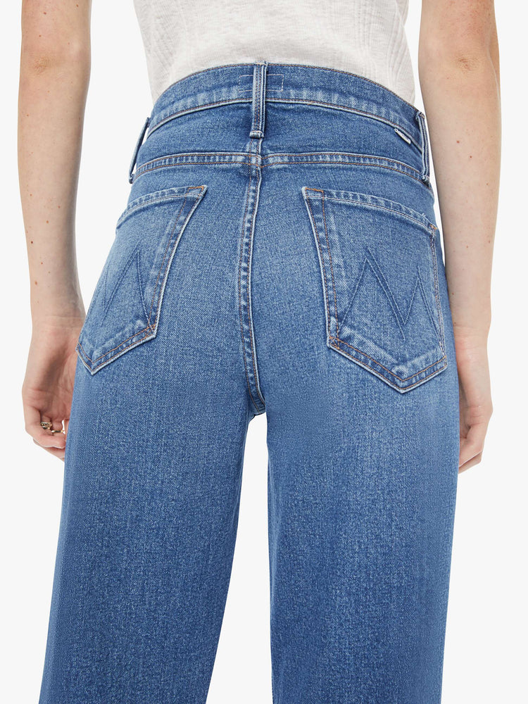 Back close up view of a woman in a med blue high-rise bootcut with a zip fly, looser leg and a long 32-inch inseam with a clean hem.