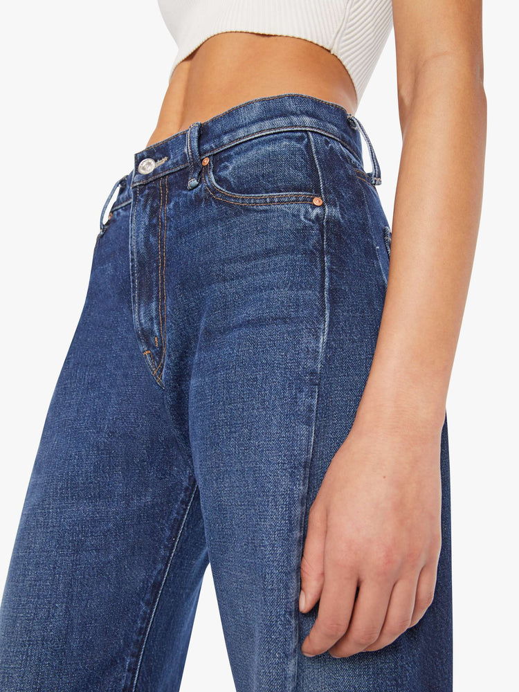 Close up view of a woman in a dark blue mid-rise jeans designed to sit lower on the hips with a full barrel leg, zip fly, 28.25-inch inseam and a frayed hem.