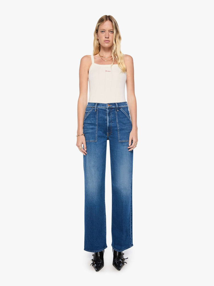 Front view of a woman in med blue super high-rise jeans with a loose fit, wide leg, patch pockets, zip fly and 34-inch inseam with a clean hem.