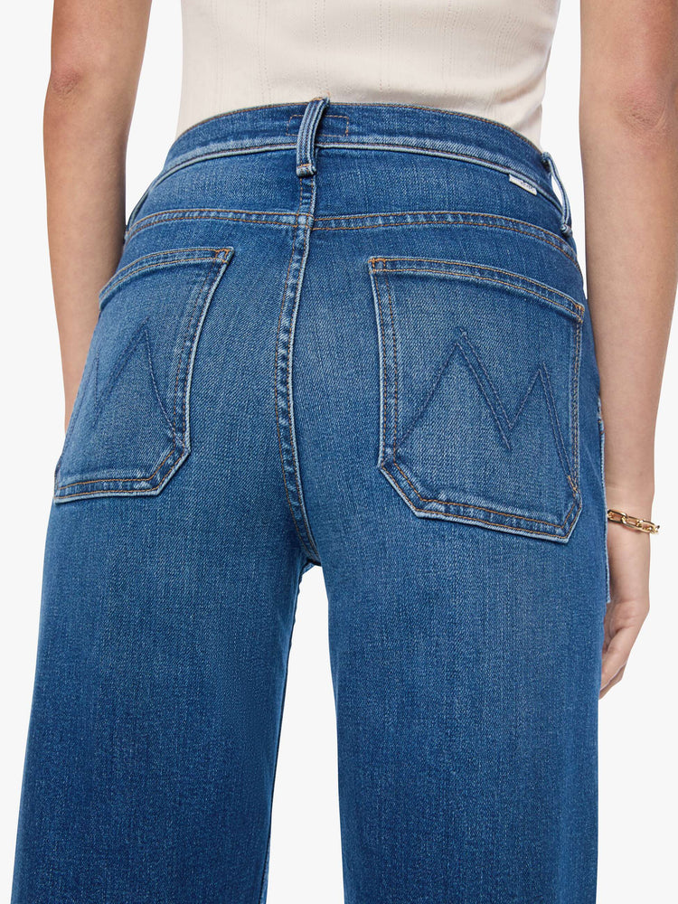 Close up view of a woman in med blue super high-rise jeans with a loose fit, wide leg, patch pockets, zip fly and 34-inch inseam with a clean hem.