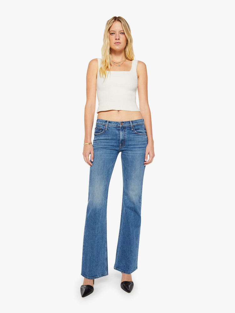 Front view of a woman in a mid blue mid-rise jeans with a flared leg, zip fly and a long 34-inch inseam with a clean hem.