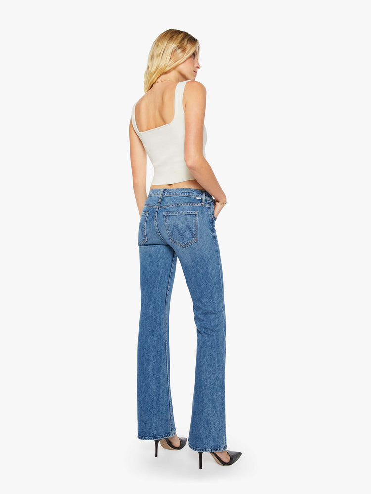 Back view of a woman in a mid blue mid-rise jeans with a flared leg, zip fly and a long 34-inch inseam with a clean hem.