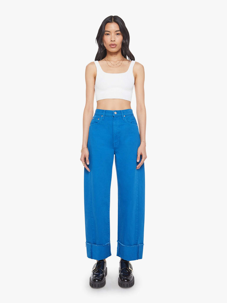 Front view of a woman in a bright blue super high-waisted pant with a zip fly, wide, curved leg and an ankle-length inseam with a cuffed, frayed hem.