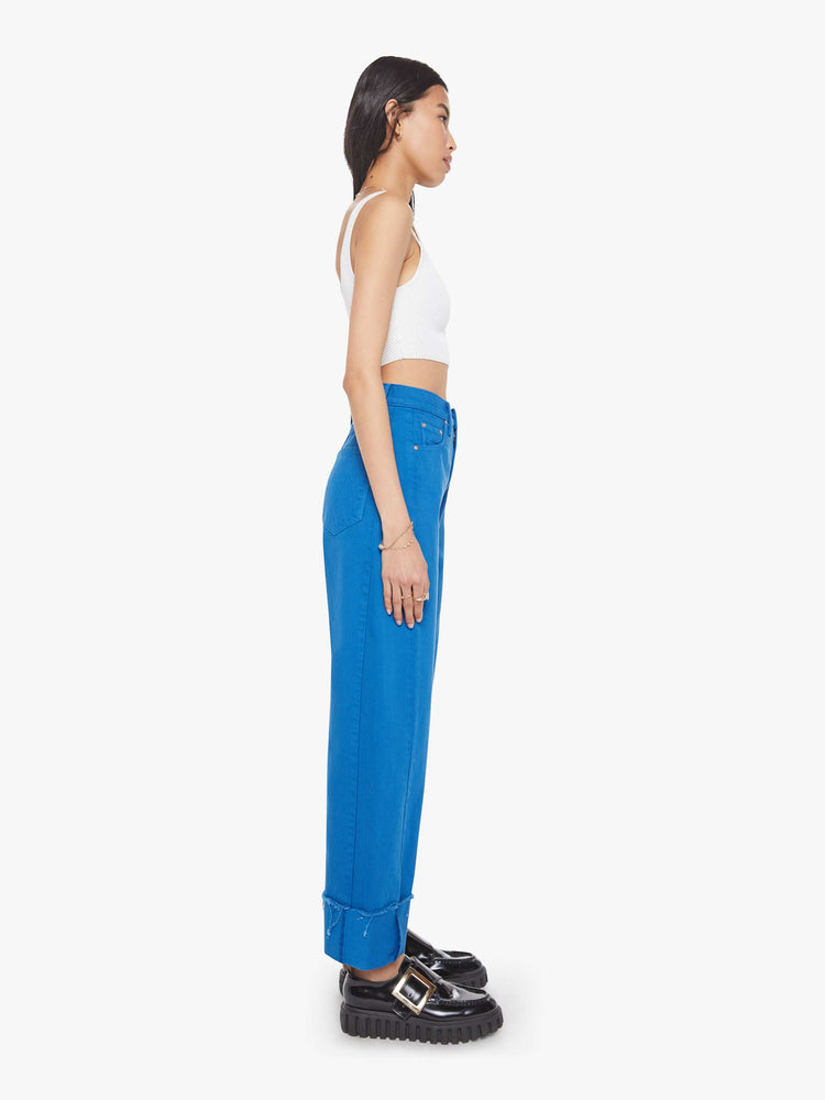 Side view of a woman in a bright blue super high-waisted pant with a zip fly, wide, curved leg and an ankle-length inseam with a cuffed, frayed hem.