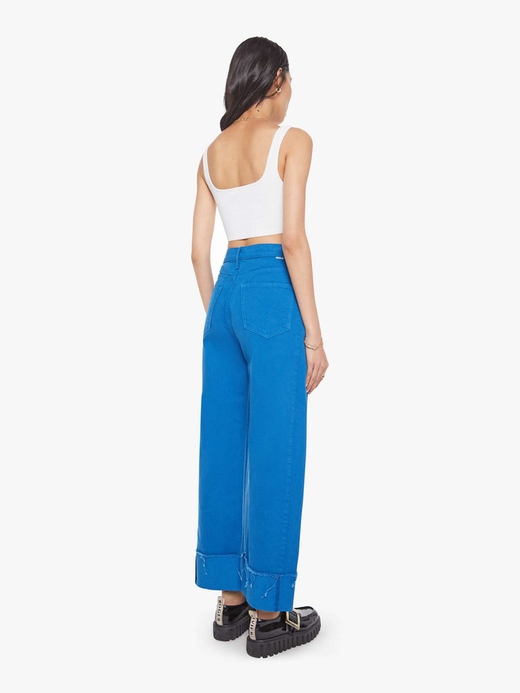 Back view of a woman in a bright blue super high-waisted pant with a zip fly, wide, curved leg and an ankle-length inseam with a cuffed, frayed hem.