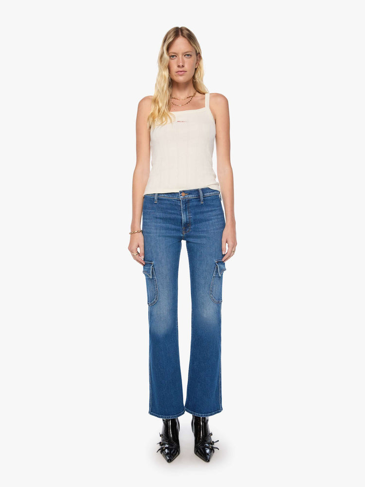 Front view of a woman in a med blue high-rise flare has a zip fly, patch pockets on the thighs, a curved seam across the back, 31-inch inseam and a clean hem. 