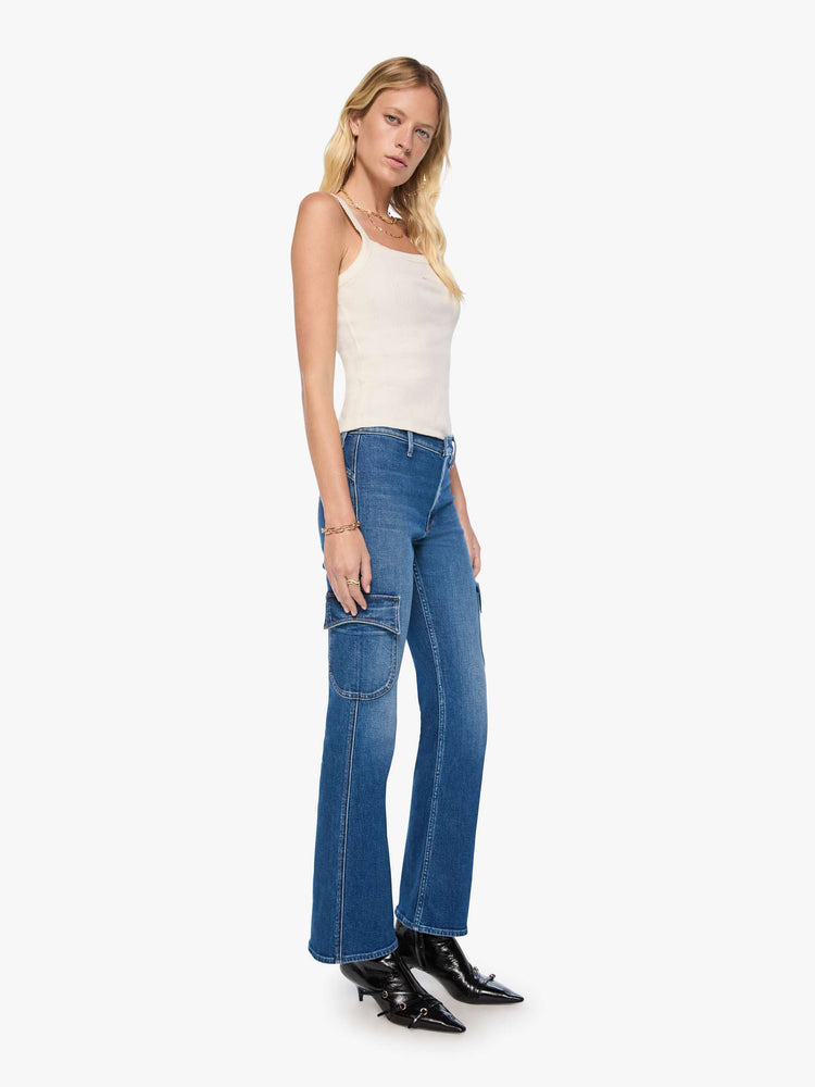 Side angle view of a woman in a med blue high-rise flare has a zip fly, patch pockets on the thighs, a curved seam across the back, 31-inch inseam and a clean hem. 