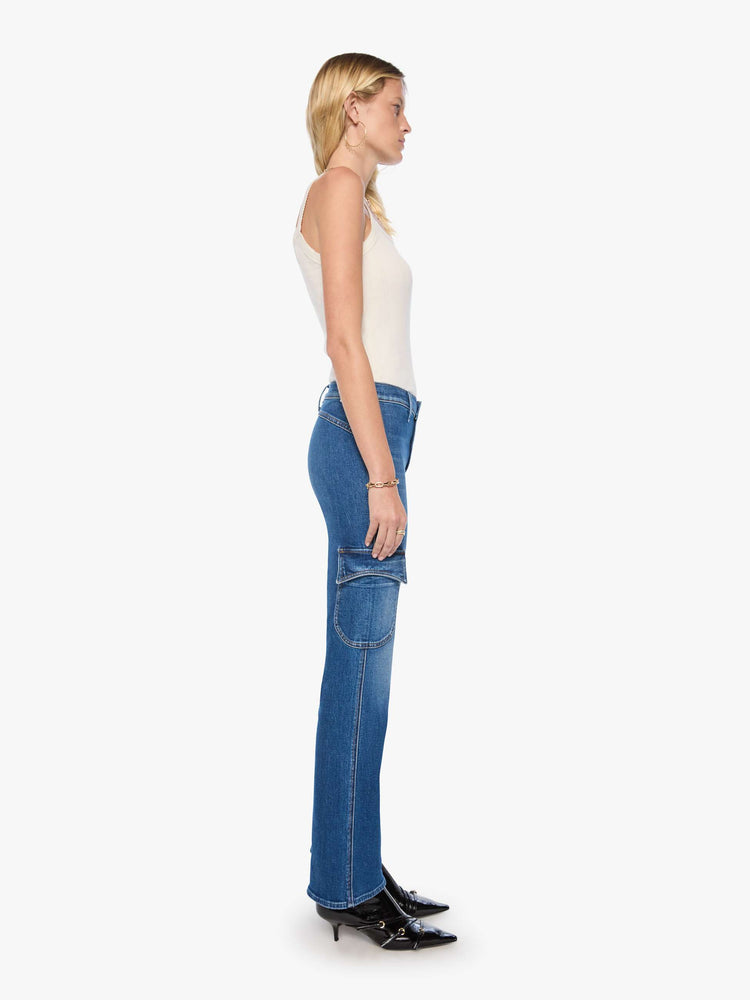 Side view of a woman in a med blue high-rise flare has a zip fly, patch pockets on the thighs, a curved seam across the back, 31-inch inseam and a clean hem. 