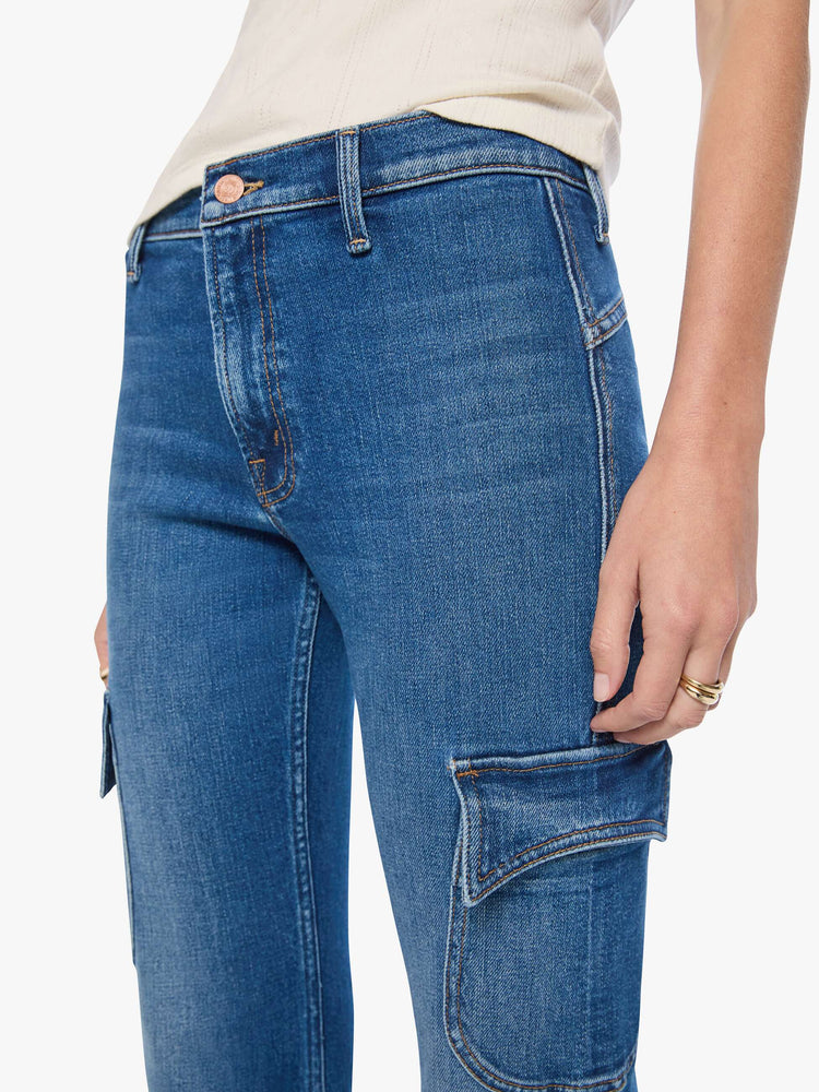 Close up view of a woman in a med blue high-rise flare has a zip fly, patch pockets on the thighs, a curved seam across the back, 31-inch inseam and a clean hem. 