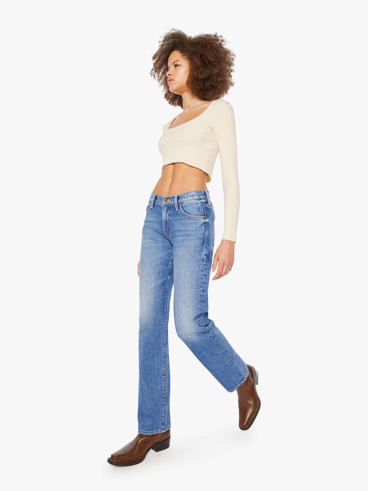 Walking view a woman in a lower-rise mid blue jeans that have a narrow straight-leg and a long 32-inch inseam with a clean hem. 