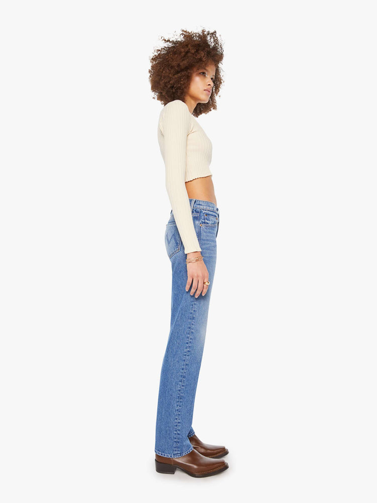 Side view a woman in a lower-rise mid blue jeans that have a narrow straight-leg and a long 32-inch inseam with a clean hem. 