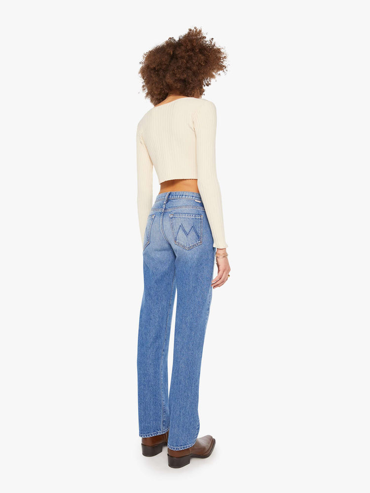 Back view a woman in a lower-rise mid blue jeans that have a narrow straight-leg and a long 32-inch inseam with a clean hem. 