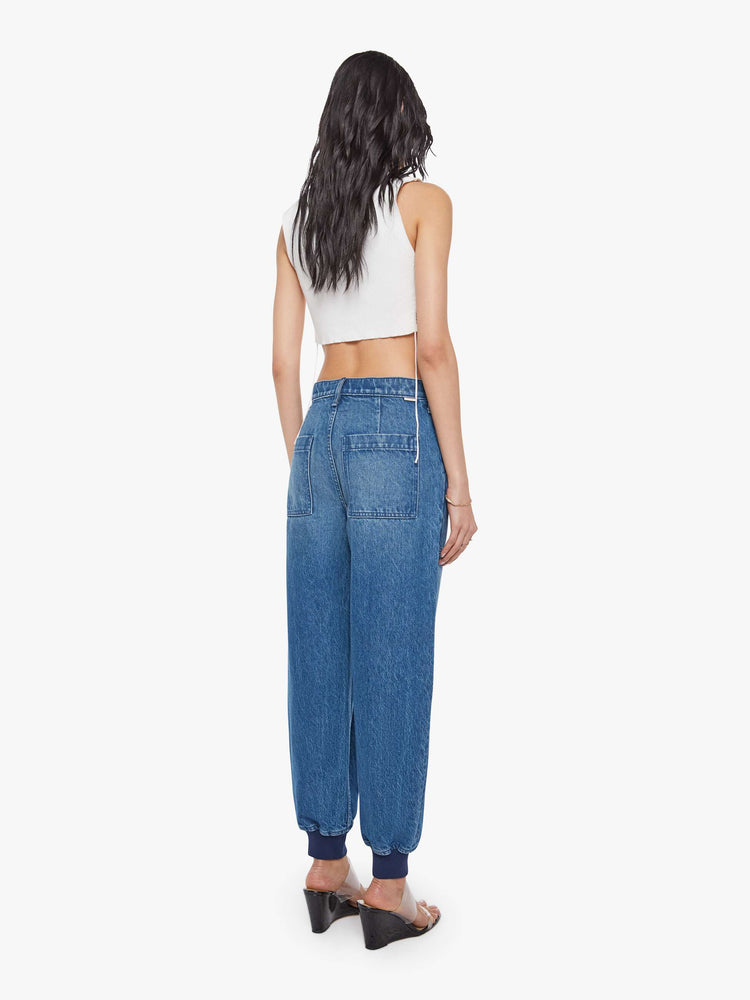 Back view of a woman in a mid blue  super high-waisted pants have a zip fly, slouchy fit designed to sit lower on the hips, oversized patch pockets and an ankle-length inseam with soft ribbed hems. 