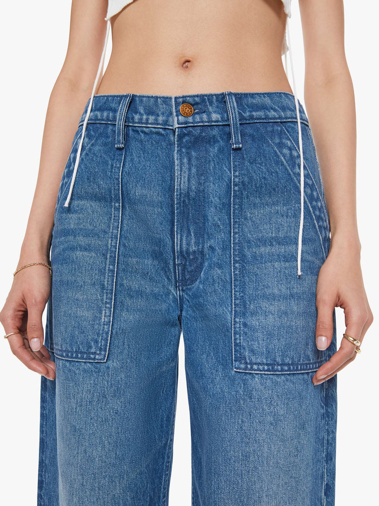 Close up view of a woman in a mid blue  super high-waisted pants have a zip fly, slouchy fit designed to sit lower on the hips, oversized patch pockets and an ankle-length inseam with soft ribbed hems. 