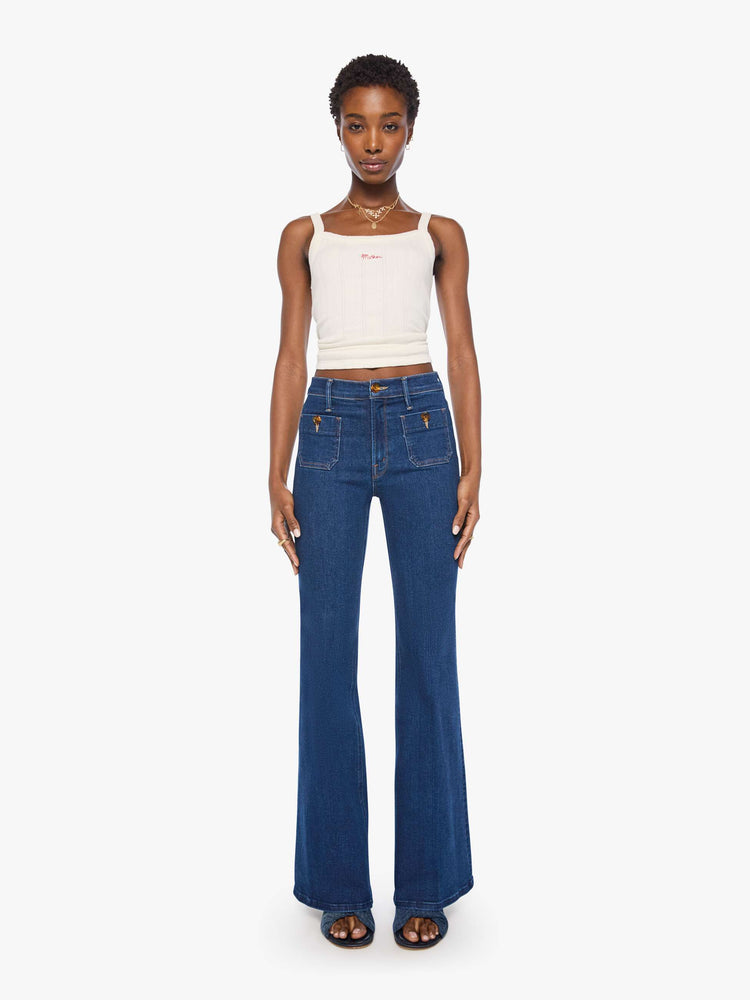 Front view of a woman in a dark blue high-rise flare with a zip fly, patch pockets that button, a long 34-inch inseam and a clean hem.