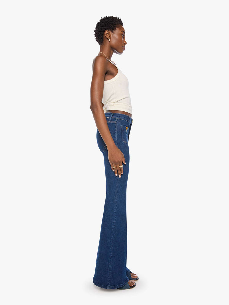 Side view of a woman in a dark blue high-rise flare with a zip fly, patch pockets that button, a long 34-inch inseam and a clean hem.