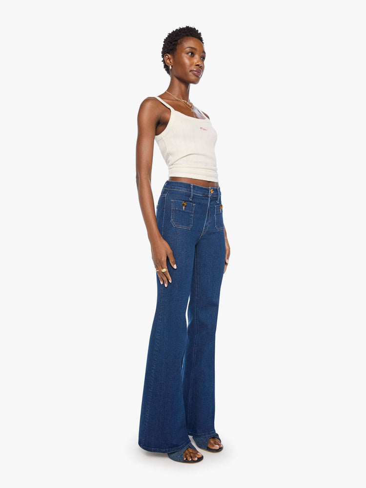 Side angle view of a woman in a dark blue high-rise flare with a zip fly, patch pockets that button, a long 34-inch inseam and a clean hem.