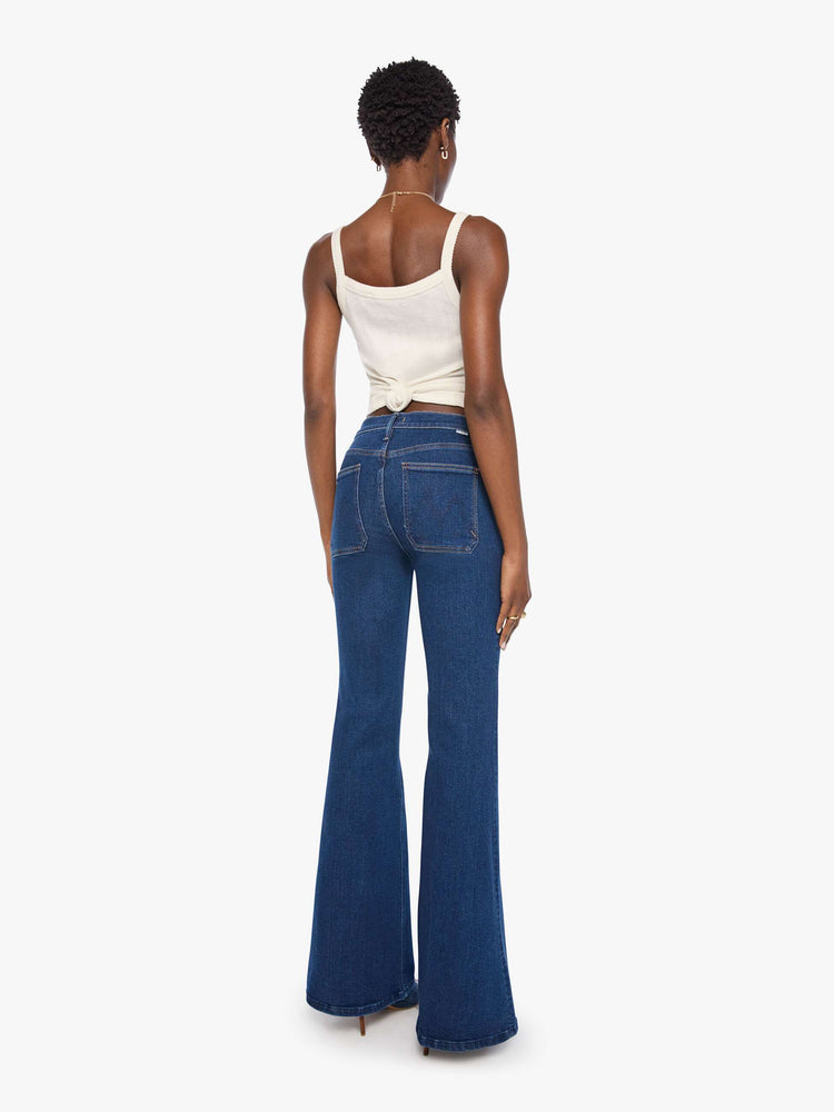 Back view of a woman in a dark blue high-rise flare with a zip fly, patch pockets that button, a long 34-inch inseam and a clean hem.