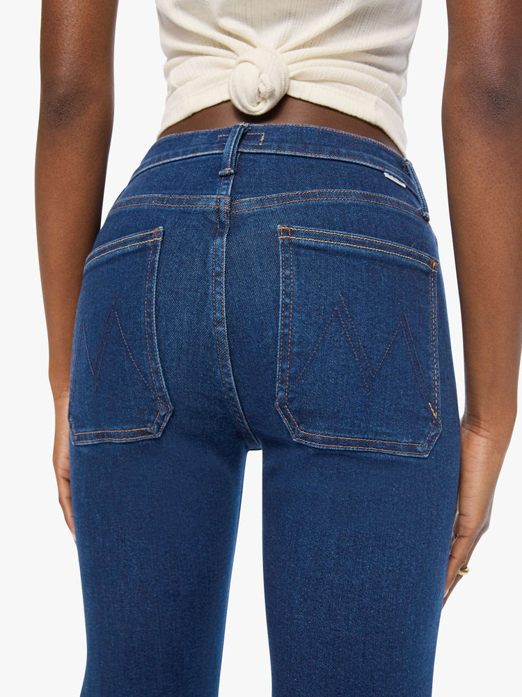 Close up view of a woman in a dark blue high-rise flare with a zip fly, patch pockets that button, a long 34-inch inseam and a clean hem.