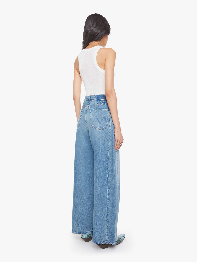 Back view of a woman in a med blue super high-waisted barrel-leg jeans with a long 32-inch inseam, a button fly, inset panels on the outer seams, a clean hem and relaxed fit.