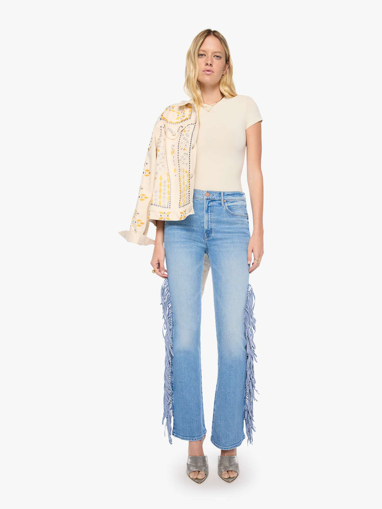 Front view of a woman in a light blue with whiskering, fading at the knees and chambray fringe along the outer leg  high-waisted bootcut jean with a zip fly, 32-inch inseam and a clean hem.