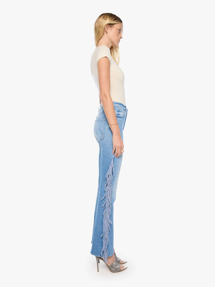 Side view of a woman in a light blue with whiskering, fading at the knees and chambray fringe along the outer leg  high-waisted bootcut jean with a zip fly, 32-inch inseam and a clean hem.