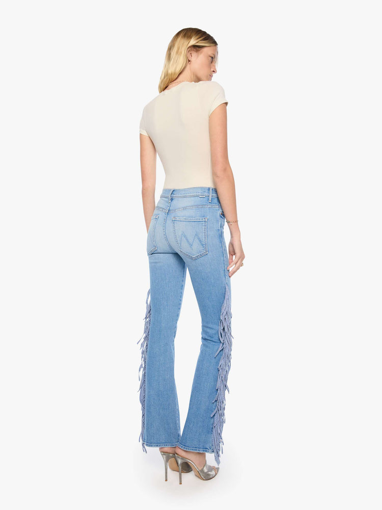 Back view of a woman in a light blue with whiskering, fading at the knees and chambray fringe along the outer leg  high-waisted bootcut jean with a zip fly, 32-inch inseam and a clean hem.