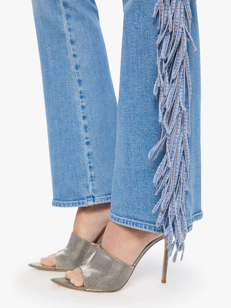 Hem view of a woman in a light blue with whiskering, fading at the knees and chambray fringe along the outer leg  high-waisted bootcut jean with a zip fly, 32-inch inseam and a clean hem.
