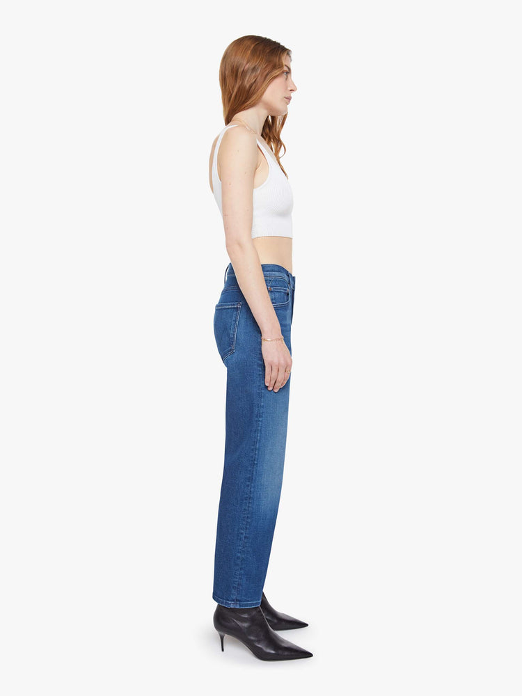 Side view of a woman in a mid blue high-rise jeans with a straight leg, zip fly and an ankle-length inseam with a clean hem.