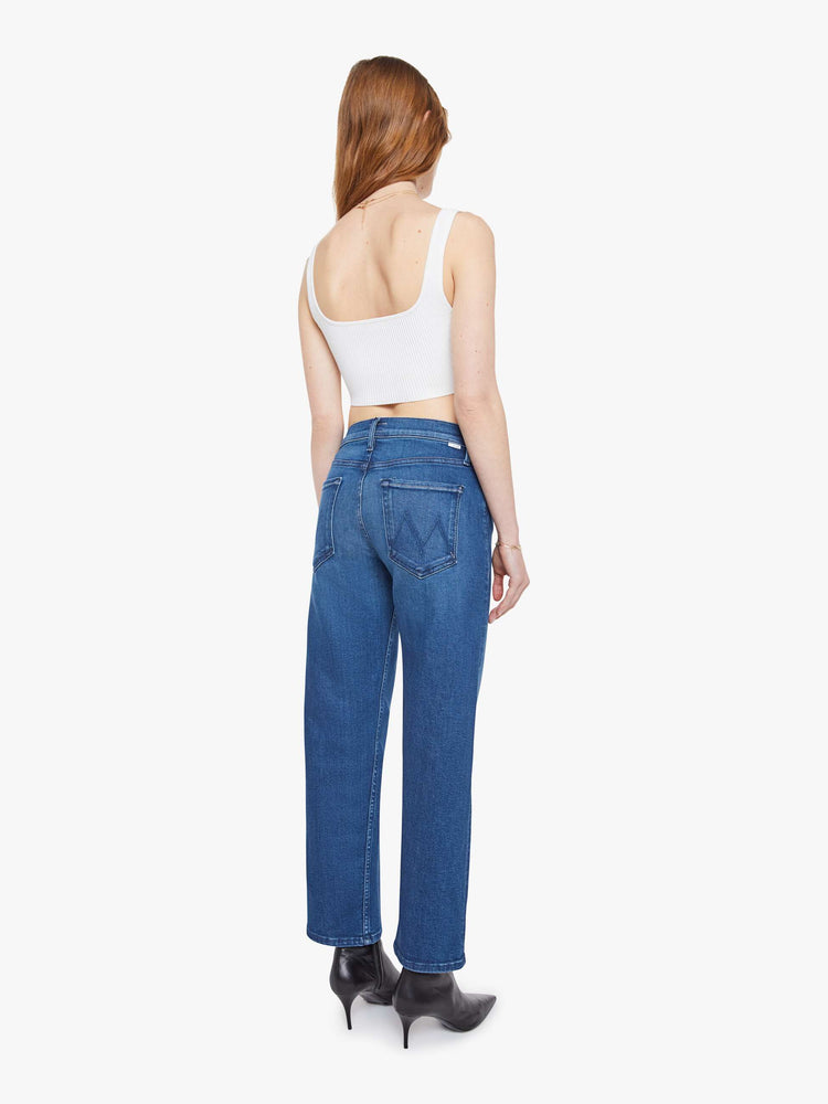 Back view of a woman in a mid blue high-rise jeans with a straight leg, zip fly and an ankle-length inseam with a clean hem.