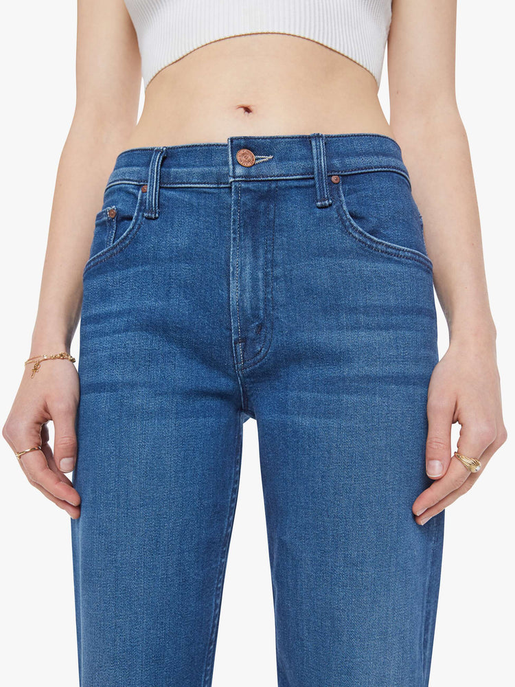 Close view of a woman in a mid blue high-rise jeans with a straight leg, zip fly and an ankle-length inseam with a clean hem.