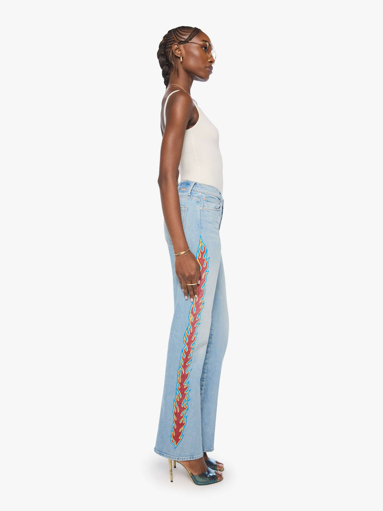Side view of a woman n a light blue denim with flame on the side bootcut jeans with a high rise, zip fly and seamless finish on the outer leg.