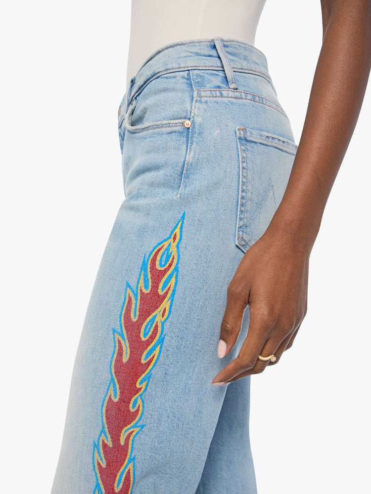 Close up view of a woman n a light blue denim with flame on the side bootcut jeans with a high rise, zip fly and seamless finish on the outer leg.