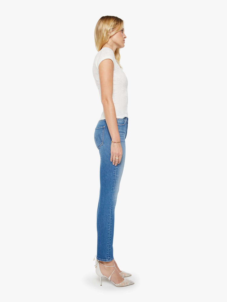 Side view of a woman in a mid blue mid-rise jean has a straight leg, zip fly, 29-inch inseam and a clean hem.