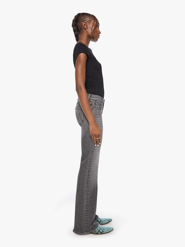 Side view of a woman in wash dark grey lower-rise bootcut jean with a long 32-inch inseam and a clean hem.