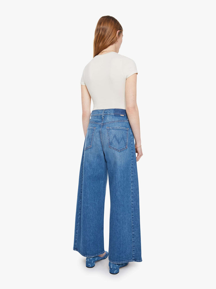 Back view of a woman in a mid-blue super high-waisted barrel-leg jeans with an ankle-length inseam, zip fly, clean hem and relaxed fit.