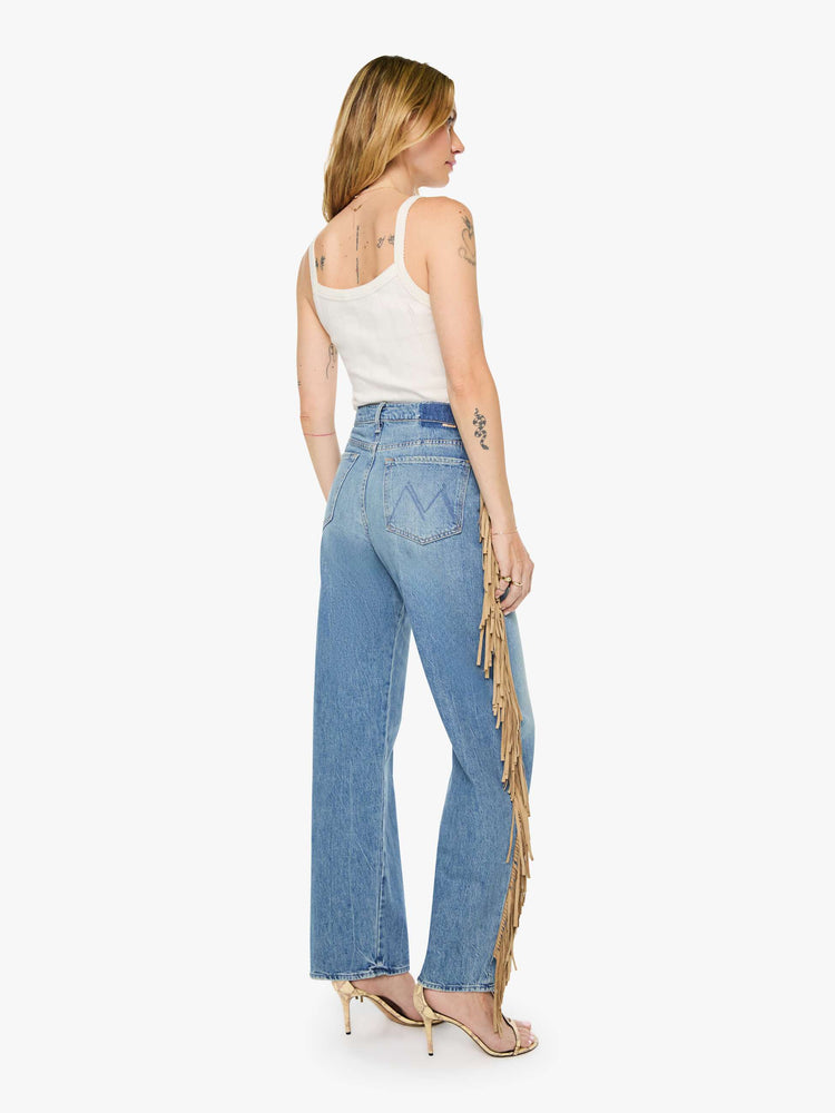 Back view of a woman in a mid blue with whiskering, fading at the knees and faux-suede fringe down the outer seam super high-waisted jean with a wide, curved leg, button fly, long 32-inch inseam and a clean hem. 