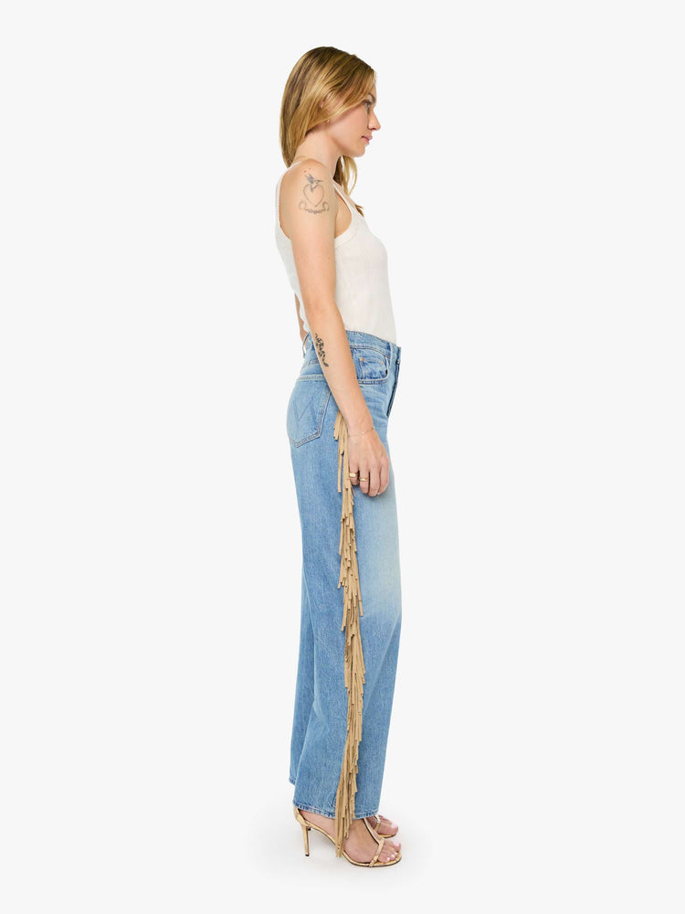 Side view of a woman in a mid blue with whiskering, fading at the knees and faux-suede fringe down the outer seam super high-waisted jean with a wide, curved leg, button fly, long 32-inch inseam and a clean hem. 